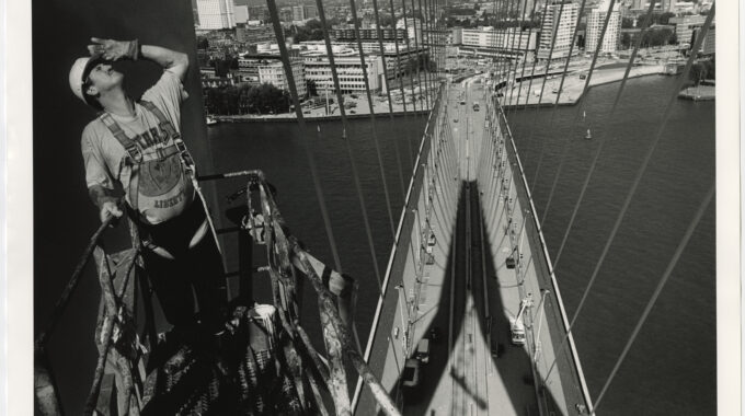 Een schilder bij de pyloon van de Erasmusbrug in aanbouw. Op de achtergrond de brug in noordelijke richting en de Rechter Maasoever.